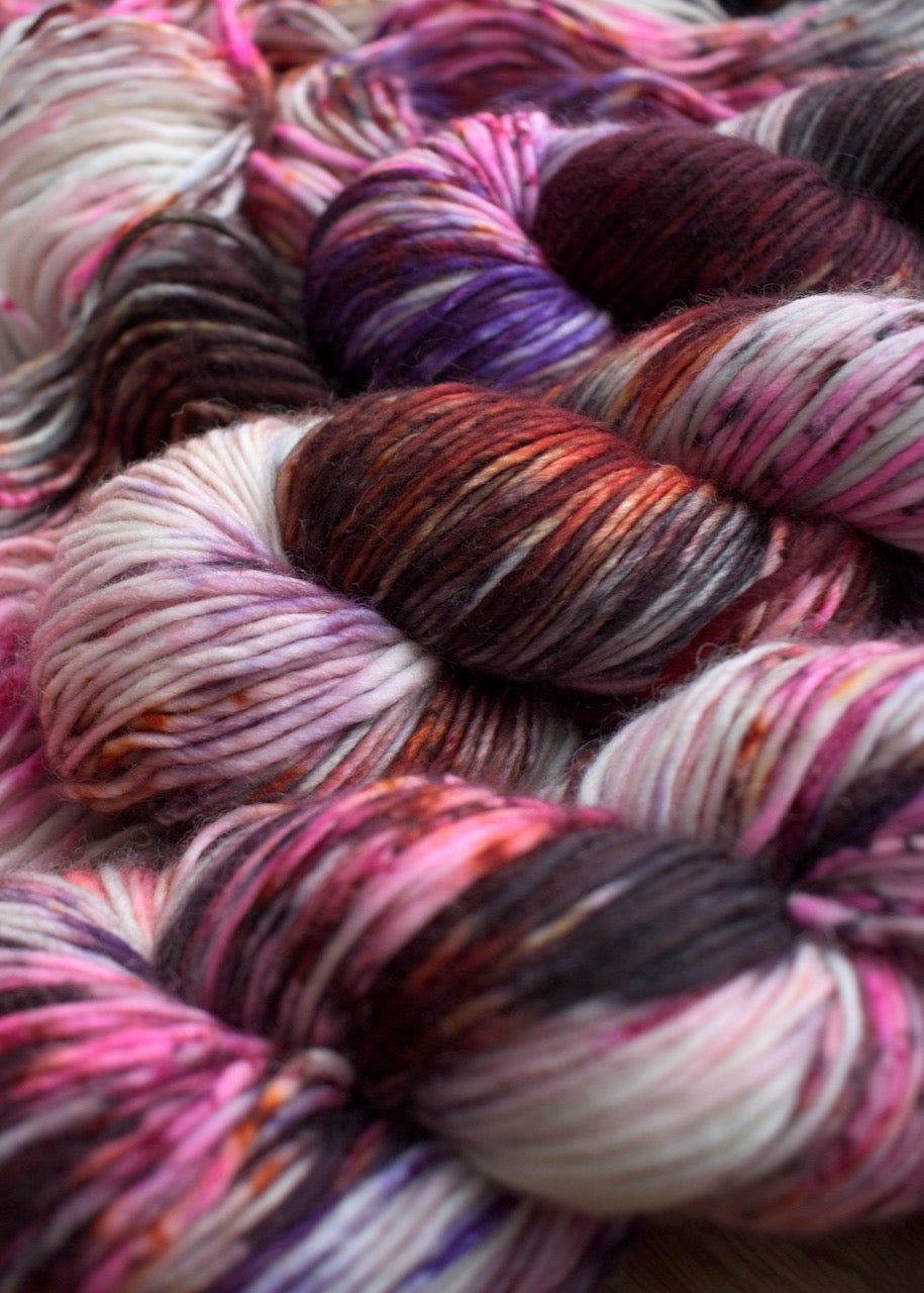 Red and purple speckled hand dyed single ply merino worsted yarn.