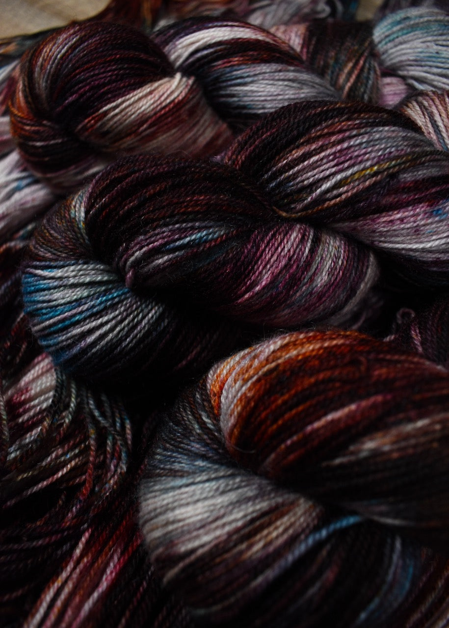 Hand dyed wool sock yarn with blue and red speckles.