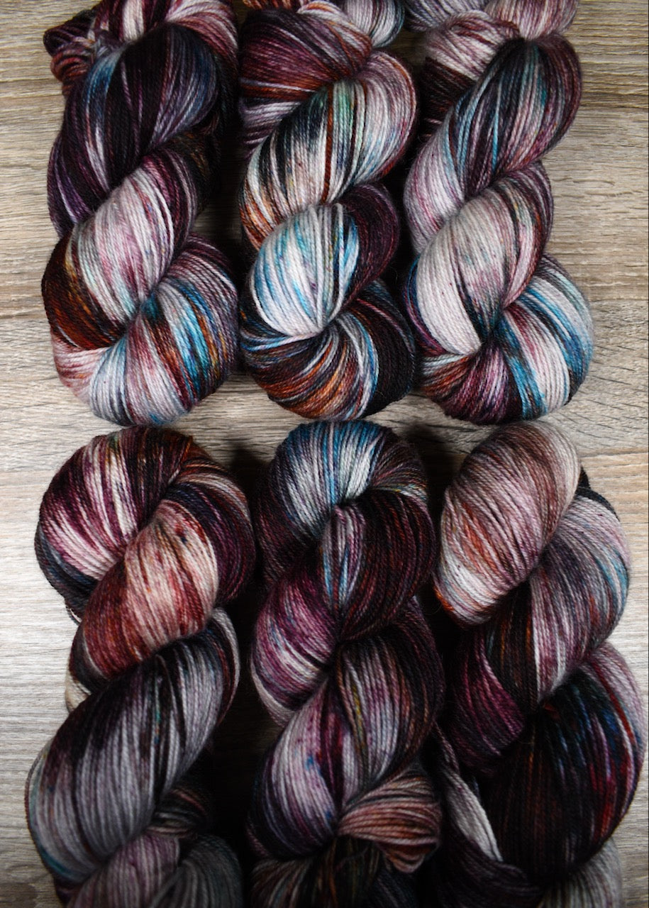 Hand dyed wool sock yarn with blue and red speckles.