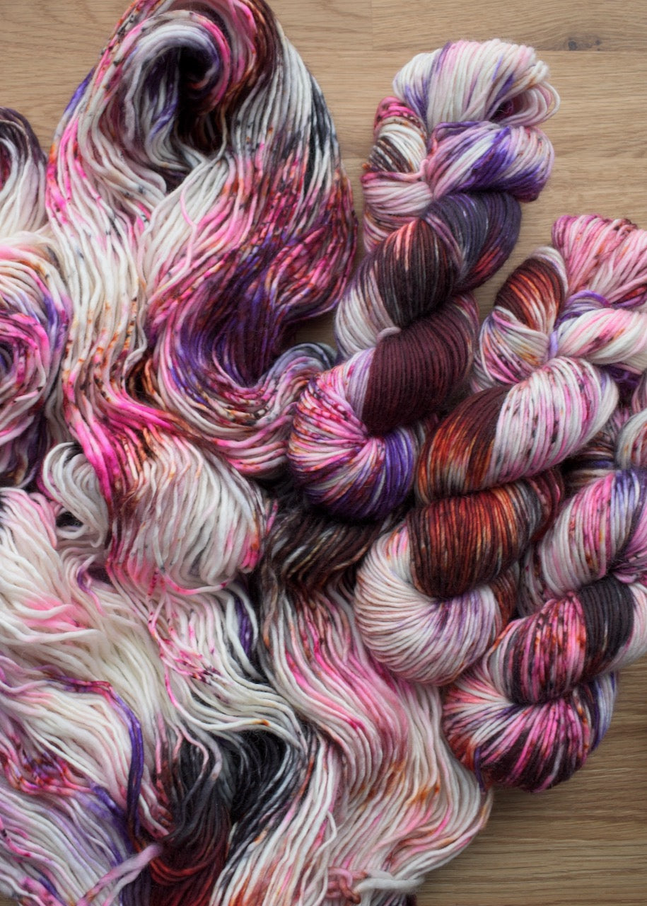 Red and purple speckled hand dyed single ply merino worsted yarn.